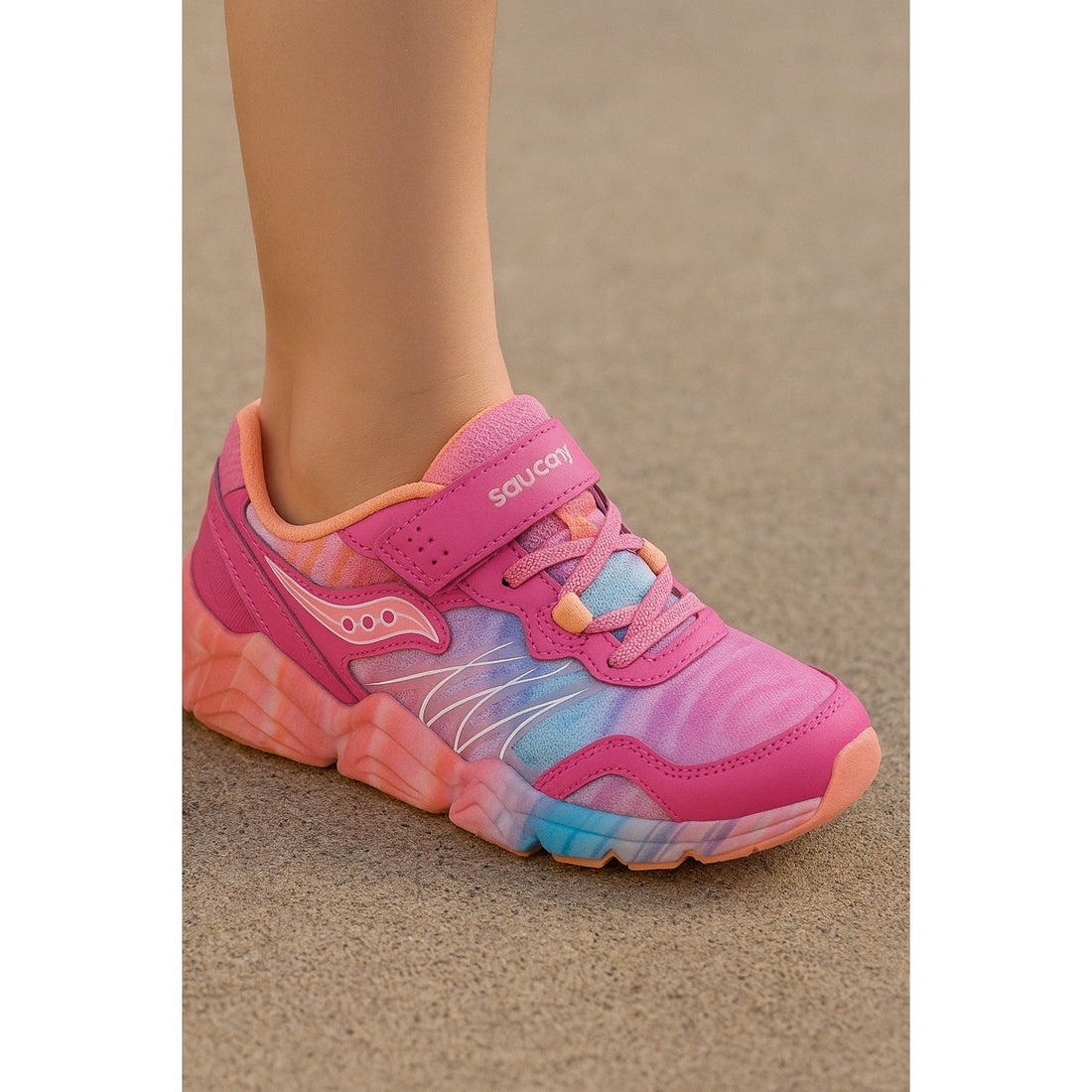 Pink and blue sneaker with 'Saucony' branding on a beige background